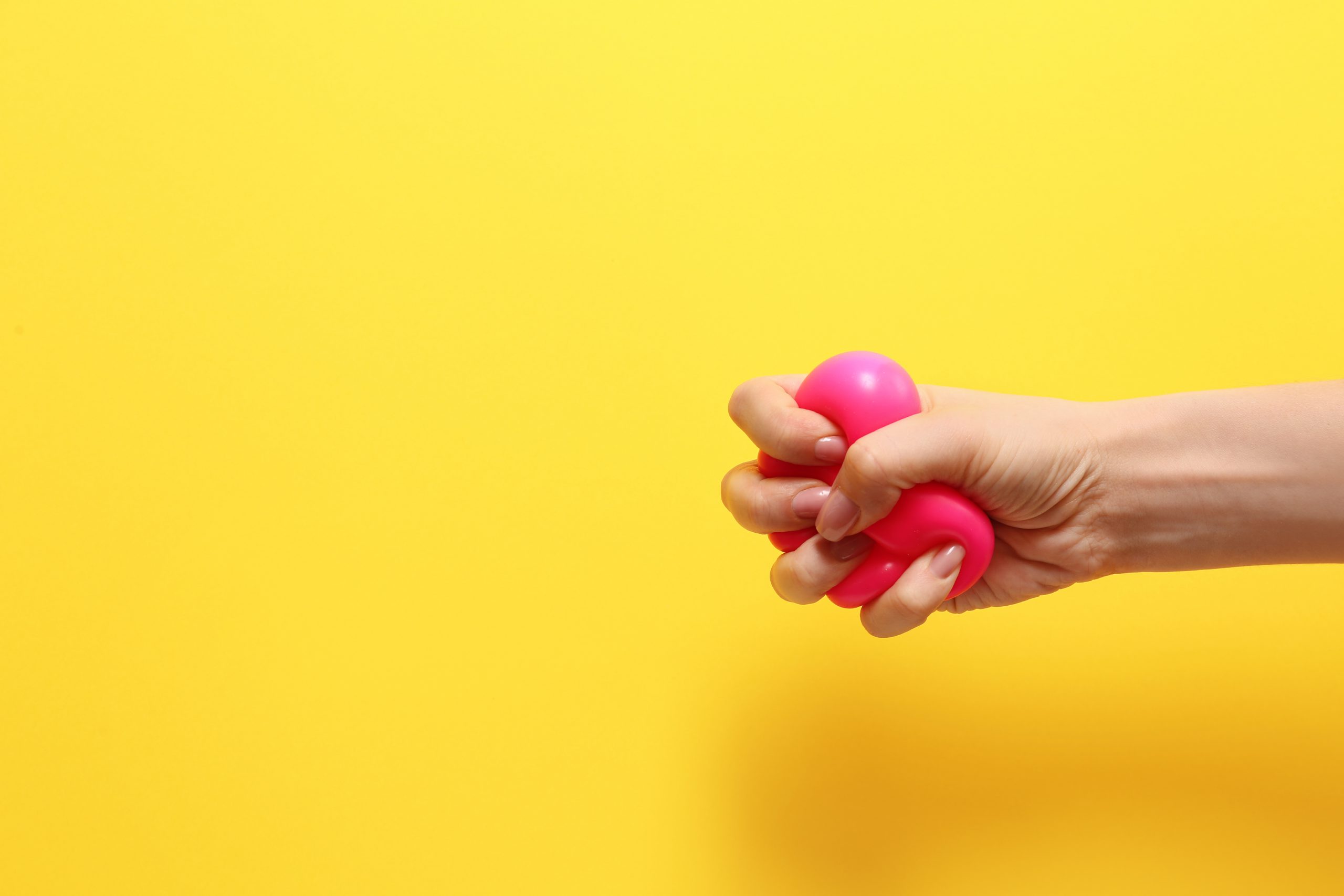 Main féminine serrant une balle anti-stress sur un fond coloré.