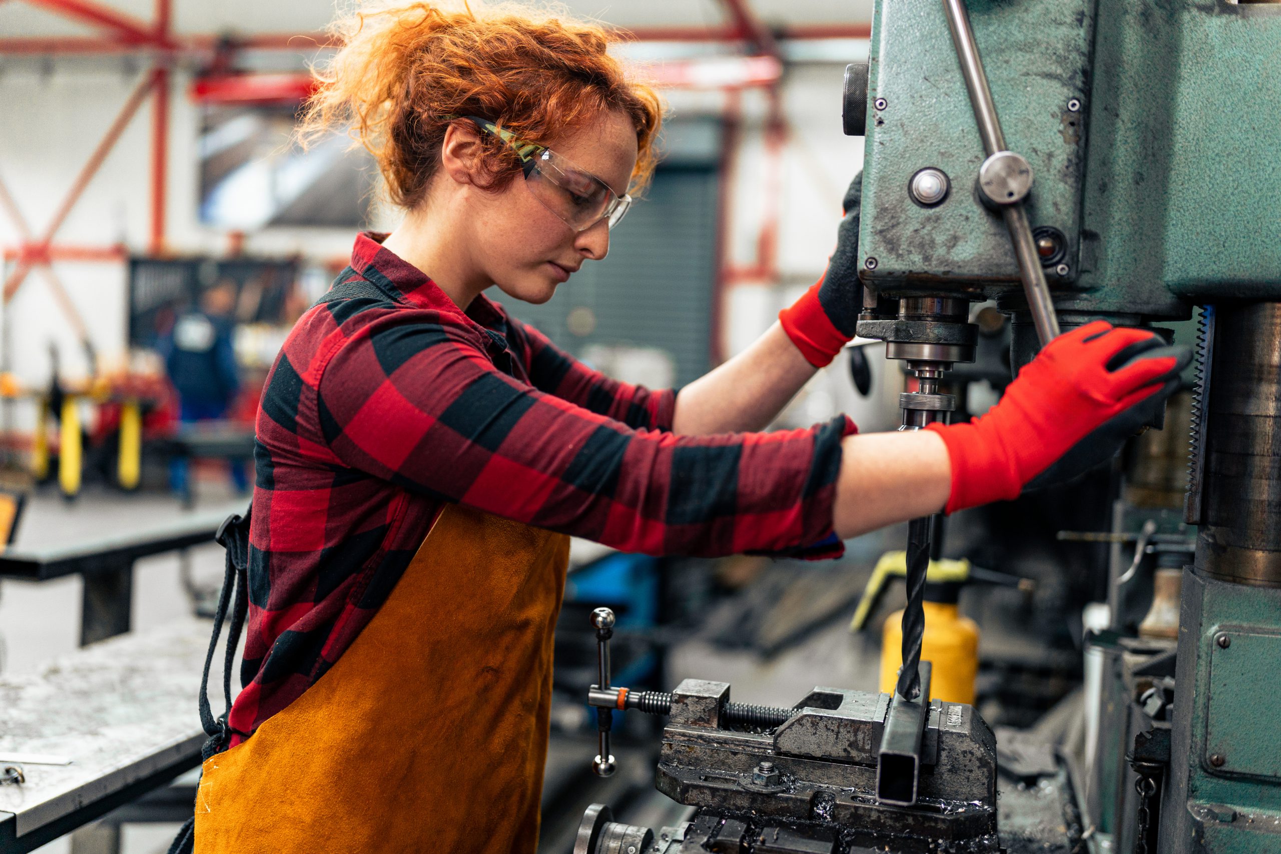 Une jeune femme dans les domaines des sciences, de la technologie, de l'ingénierie et des mathématiques ajuste une machine avec une perceuse avant de commencer à travailler sur un nouveau projet. Elle utilise un équipement de protection et respecte les règles de sécurité au travail.